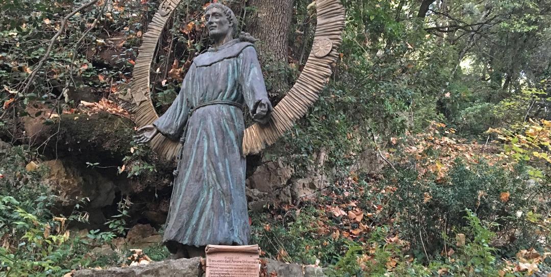 Statue des Heiligen Franziskus, umgeben von Grün, mit offenen Armen als Zeichen der Gastfreundschaft und Spiritualität.