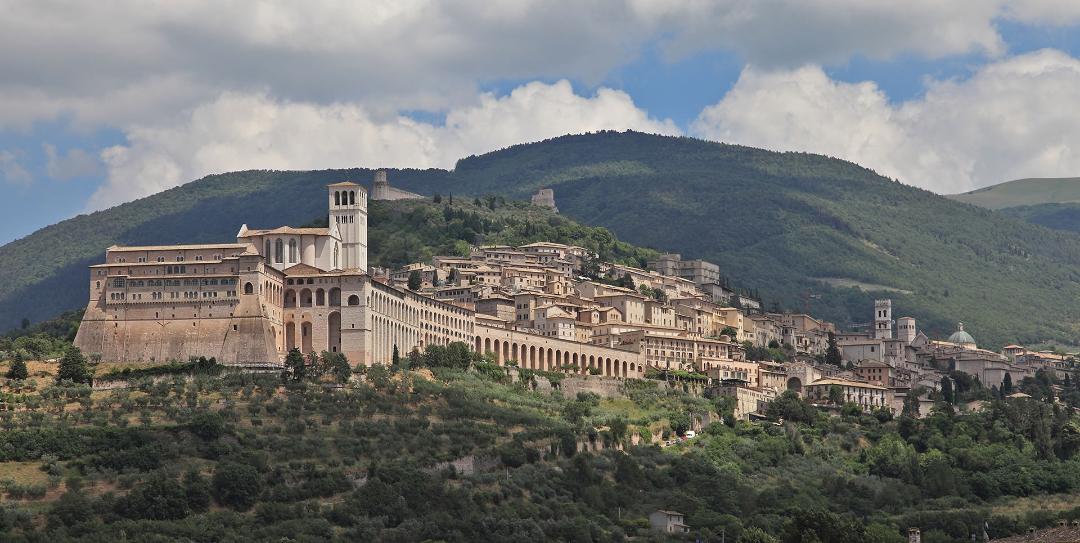 Vista panoramica di Assisi con la Basilica di San Francesco in primo piano ed edifici storici. Sullo sfondo il Monte Subasio