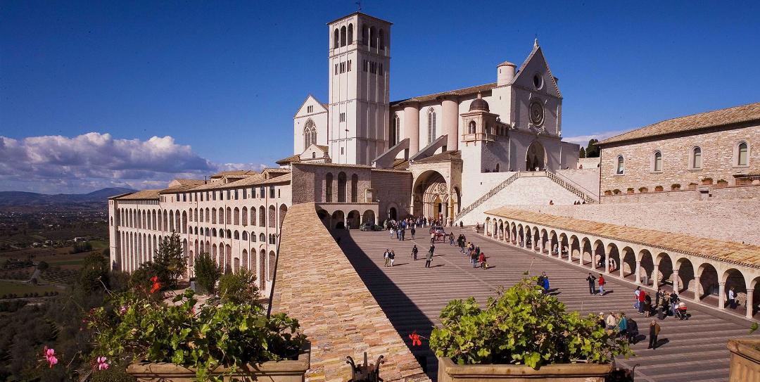 Basilica di San Francesco ad Assisi con la sua imponente scalinata e arcate, con visitatori in una giornata soleggiata